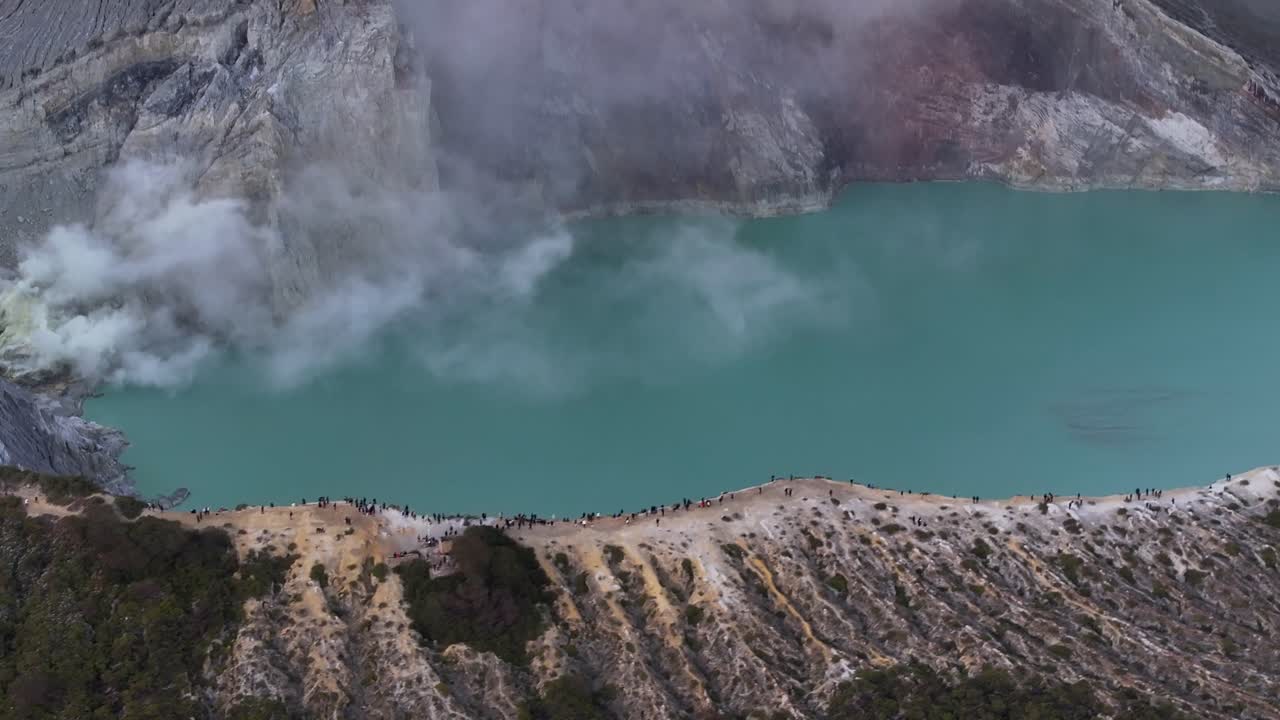 un primer plano aéreo de personas en el borde del cráter viendo el humo que sale del volcán ijen en indonesia.