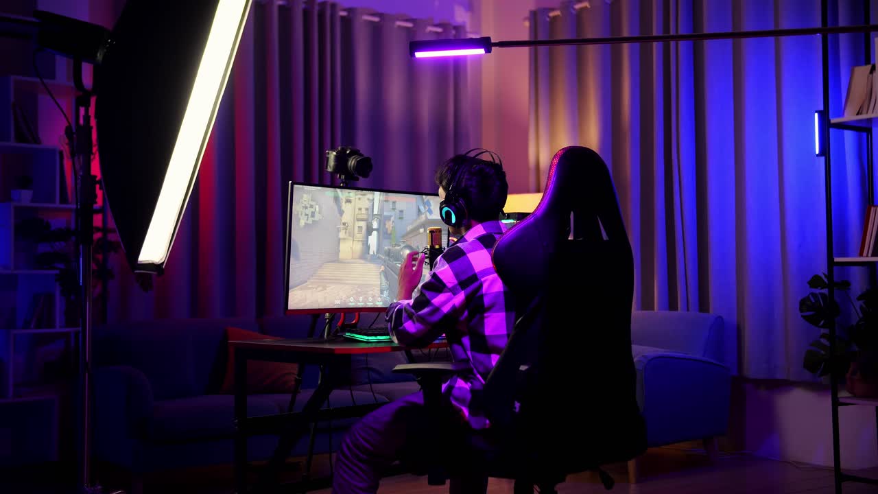 Back View Of Asian Boy Streamer Playing Game Over Network On Personal Computer. Challenge And Bully Competitor, Live Stream Video Game, Desk Illuminated By Rgb Led Strip Light