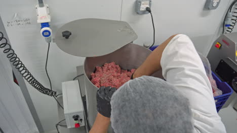 over the shoulder shot of a man filling an industrial mincer with raw meat