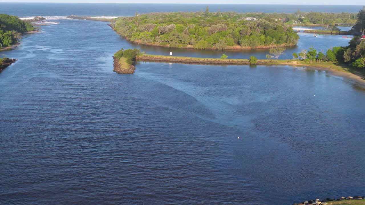 Drone footage captures a serene river and lush greenery under clear skies at Brunswick Heads, NSW, Australia