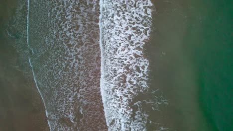 waves crashing into sand from an aerial view