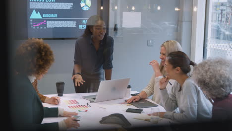 view through glass of businesswomen collaborating in creative meeting around table in modern office