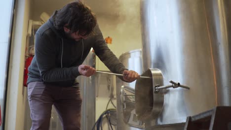 beer production - brewer pulls out spent malt from a beer brewing tank in the brewery - side view slowmo