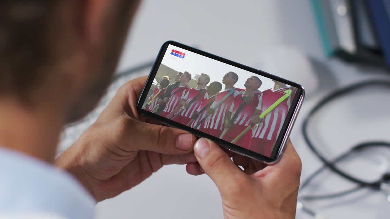 compuesto de un médico masculino viendo un partido de hockey en un teléfono inteligente