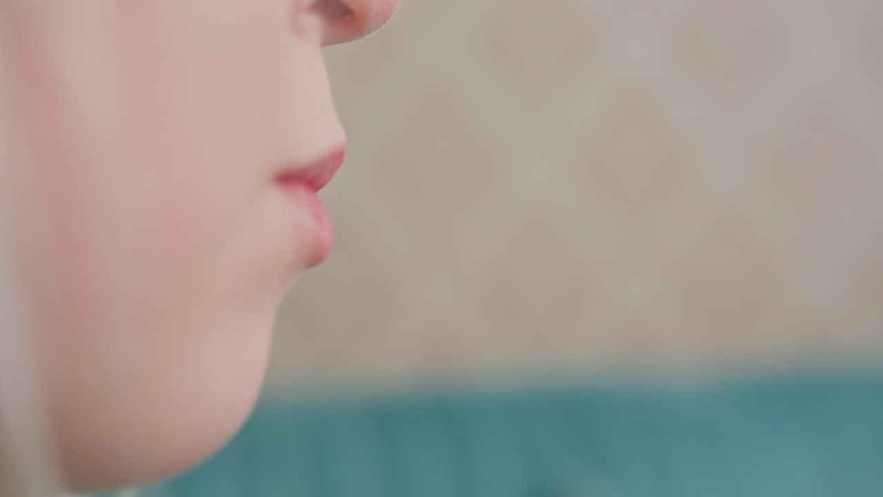 close up side view of lady eating with warm smile, relaxed indoor moment, patterned wall and green couch in background, casual home setting, natural light, happiness, comfort, leisure time