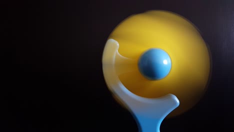 close up of a mini blue and yellow electric fan spinning on black background