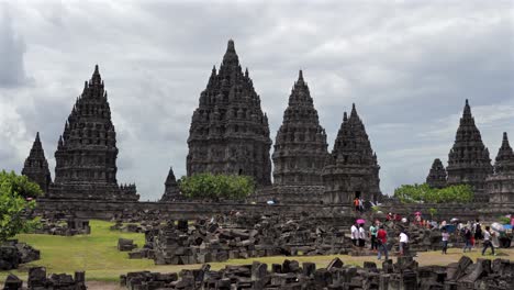 indonesia,prambanan temple on a cloudy day from a distance, covering all temples, camera moves from left to right slowly, people walking around the temple complex.