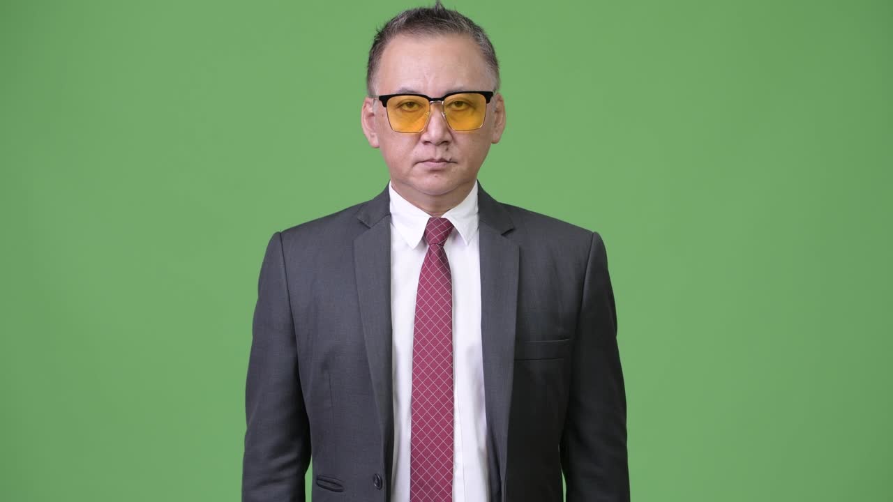 un hombre de negocios japonés maduro con gafas de sol contra un fondo verde.