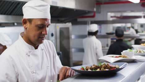 caucasian male chef garnishing dish and smiling in restaurant kitchen
