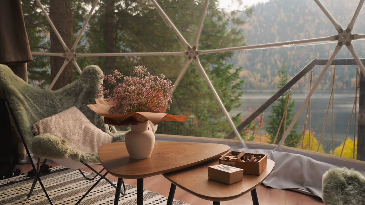 Dining table with view from window. Modern place for lunch breaks. Panoramic glass terrace of glamping hotel room overlooking wide river and dense forest
