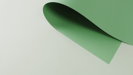 close up of green rolled piece of paper on white background with copy space in slow motion