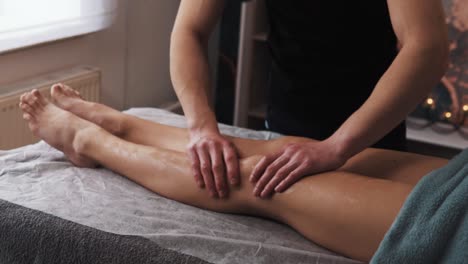 hands of a male masseur doing a gentle massage of a woman's legs in a massage room with soft light