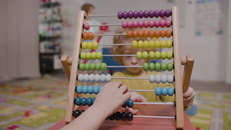 Camera-Focuses-On-The-Hands-Of-Little-Kid-Playing-With-A-Panel-Moving-Wooden-Pieces-1