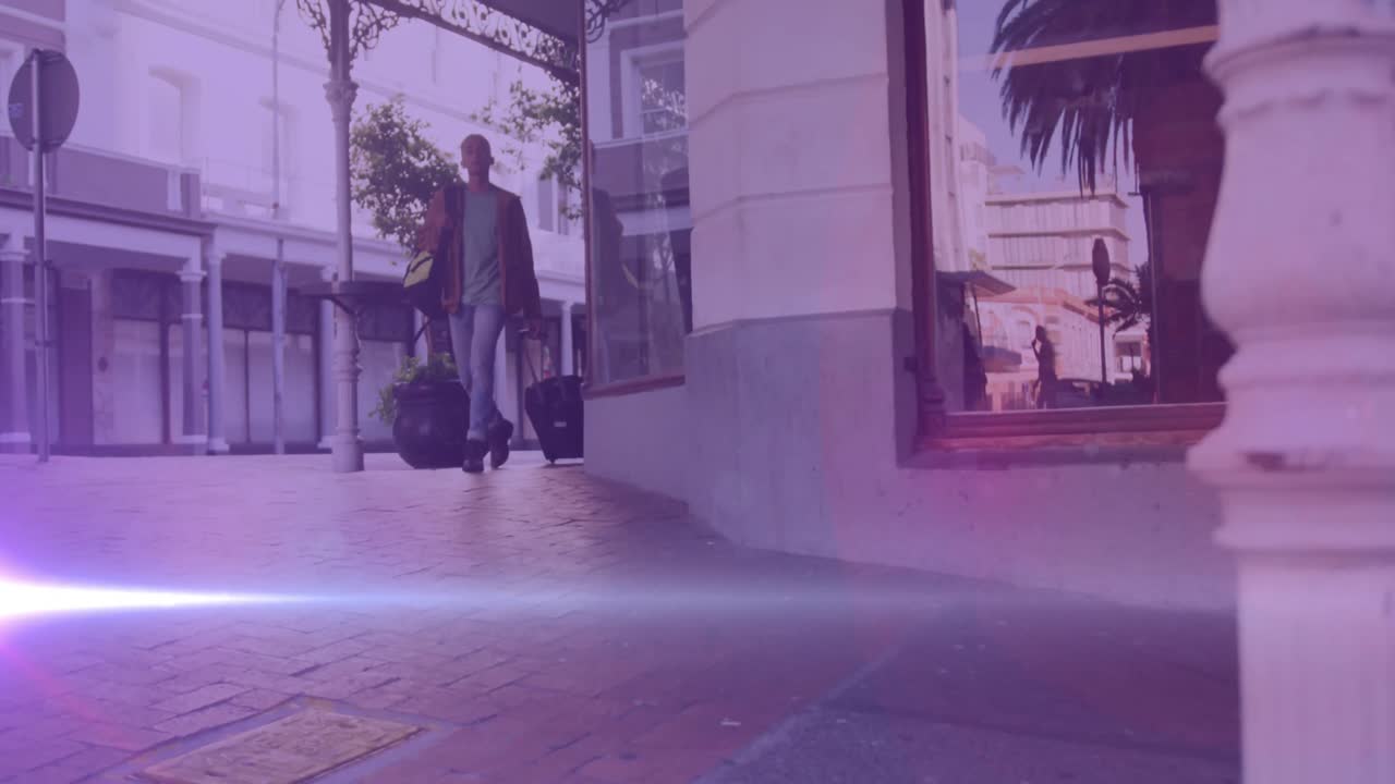 Video of coloured lights over biracial man walking to work, wheeling suitcase in street