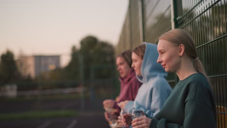 three friends resting after exercise, seated with water bottles in hand, sipping water to hydrate while enjoying a well-deserved break, background blurred, reflecting the peaceful atmosphere