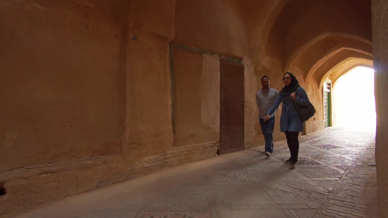 European woman with hijab walking in small mud brick alley in old city of Yazd, Southern Iran. Yazd is famous for it's wind towers or wind catchers and zoroastrian tradition.