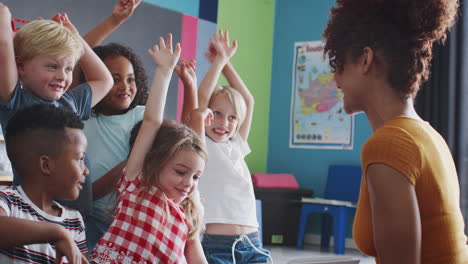 Grundschüler-Heben-Die-Hände,-Um-Fragen-Zu-Beantworten,-Während-Eine-Lehrerin-Im-Klassenzimmer-Eine-Geschichte-Vorliest