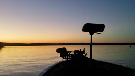 Colorful-Sun-Rise-in-Bass-Fishing-Boat-on-Calm-Beautiful-Lake,-Ripples-in-the-Water-and-Trees-in-the-Background,-Yellow-and-Purple,-Pan-Right