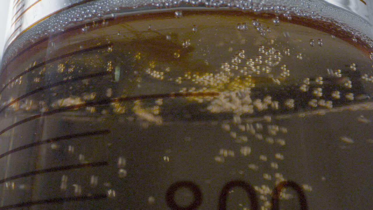 Close up of a drop of colored liquid descending from a test tube into a gaseous liquid in a laboratory setting.