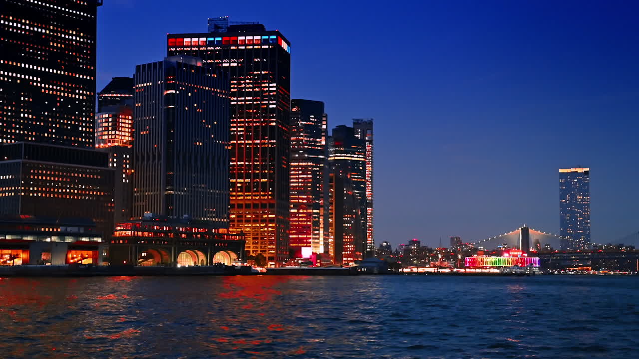 City lights of high-rise city skyline reflect in the riverscape. Boat tout by the East River at dusk time. The Brooklyn Bridge with illumination at backdrop