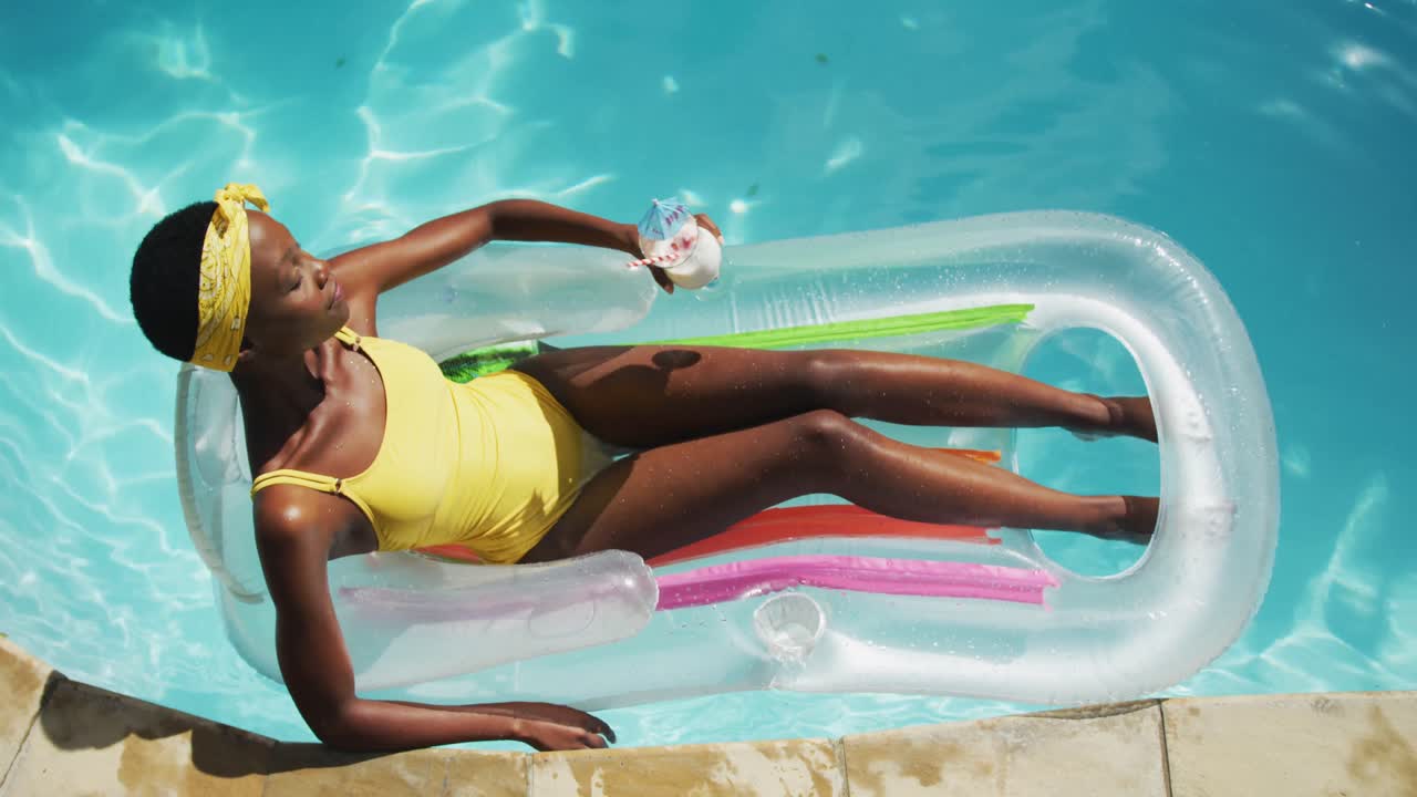 Attractive african american woman lying on inflatable holding drink and sunbathing in swimming pool