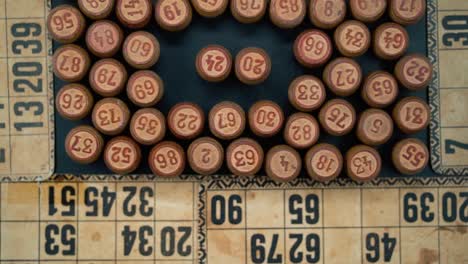 cinematic close-up smooth shot from above of a pile of bingo wooden barrels in a square, woody figures, old numbers background, vintage board game, slow motion 120 fps zoom out gimbal video