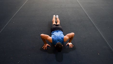 a guy doing a special kind of push up in a top-side-front view still shot inside a gymnastics gym