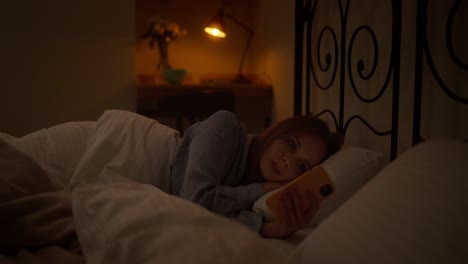 woman using phone in bed at night