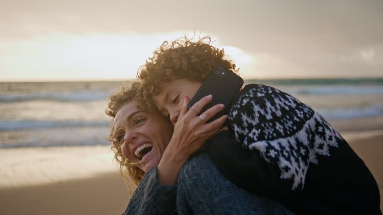 niño lindo hablando por teléfono en vacaciones en la costa con la madre de cerca. familia feliz habla