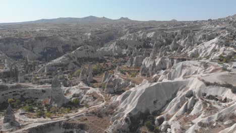 Wide-aerial-view-of-deep-valley-and-rock-formations-dotted-with-homes,-chapels,-tombs,-temples-and-entire-subterranean-cities-carved-into-the-stone-in-Cappadocia