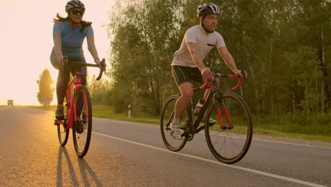 Front-view-of-a-young-couple-or-friends-riding-their-bikes-in-the-city-park-or-boulevard-in-summertime.-People-leisure-and-lifestyle-concept