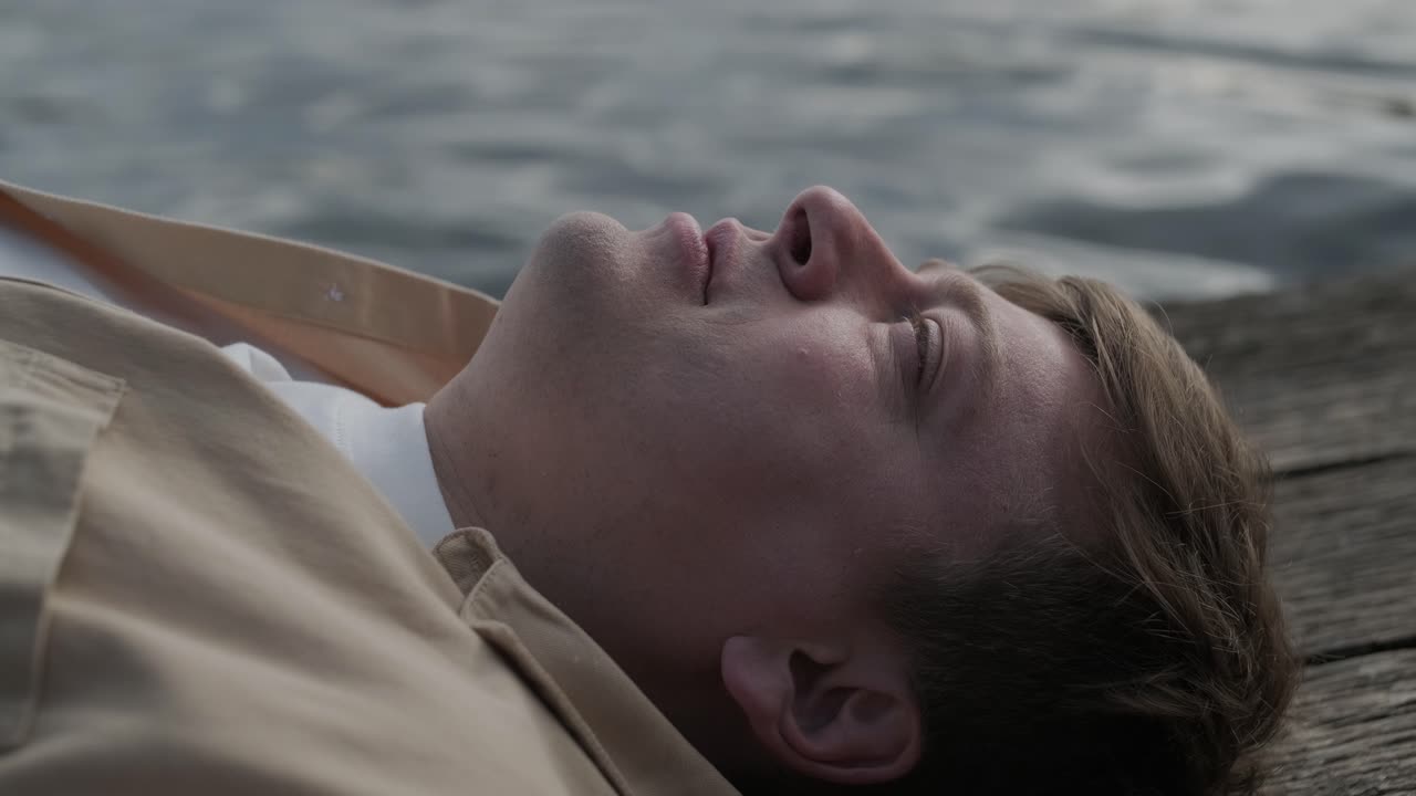 젊은이가 나무로 된 보행자 다리 위에 혼자 누워서 호수를 쳐다보고, 삶에 대해 생각하고, 자연에서 평화로운 분위기를 누리고, 신선한 공기를 즐기고, 뒤를 바라보고 있습니다.