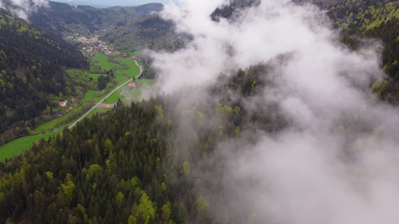Drone slow fly through thick cloud over a forest mountain valley with a rural road during spring time