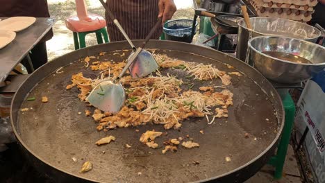 cooking noodles on a large wok outdoors.