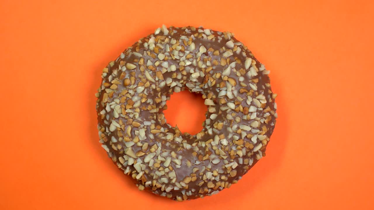 rosquilla de chocolate brillante y colorida con nueces de primer plano, macro disparado, girando sobre un fondo naranja.