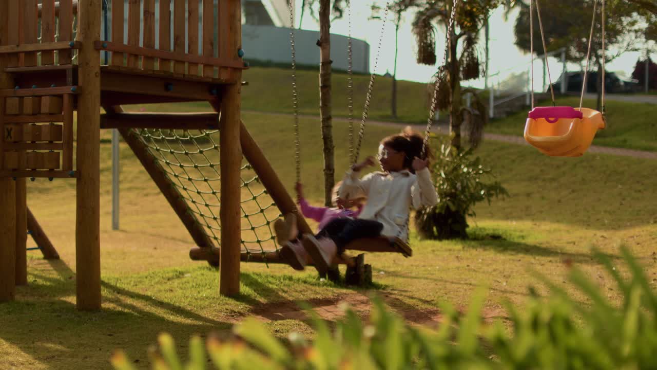 Two young girls playing on swings at a sunny playground