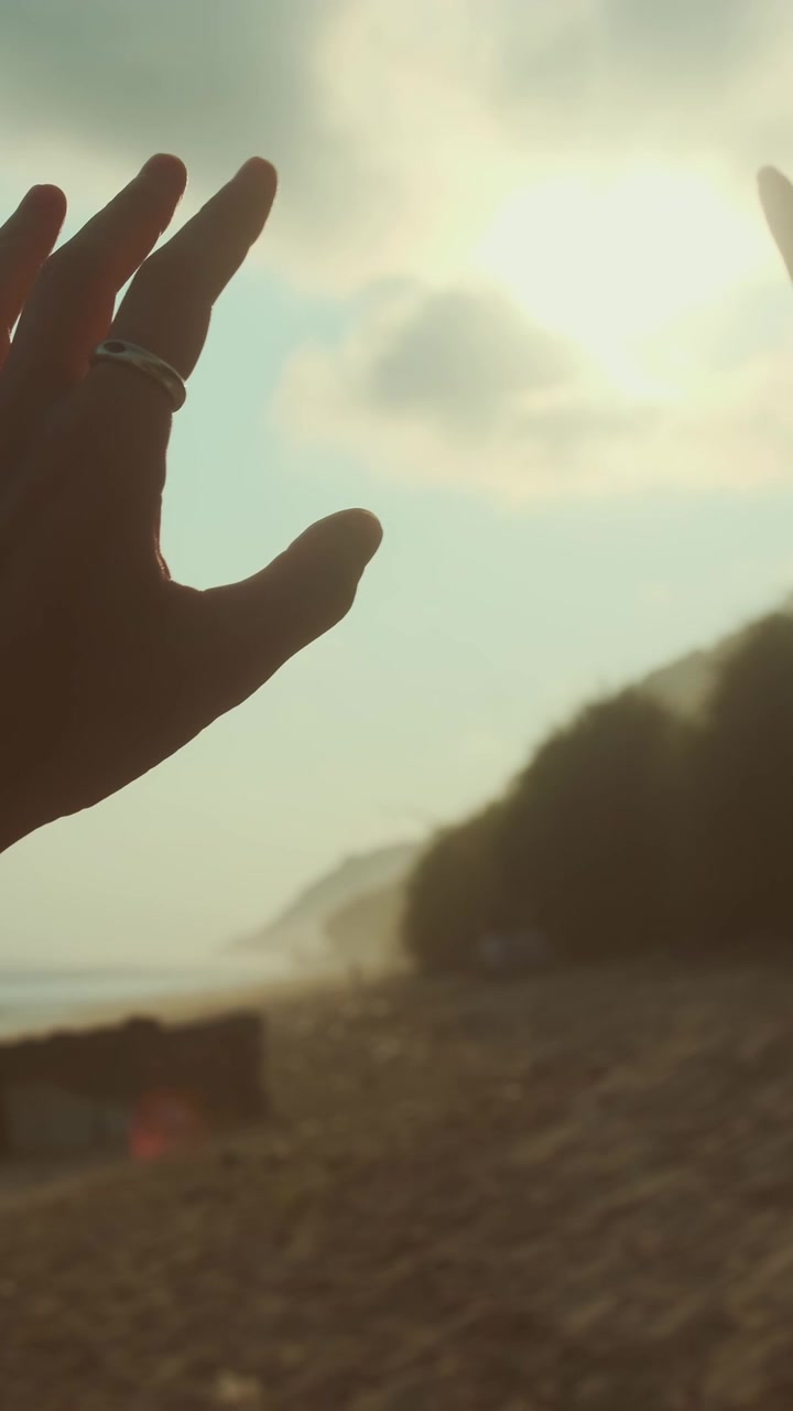 Hand reaching towards the sky near the beach at sunset