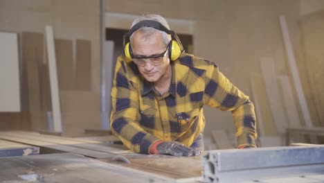 Male-carpenter-is-cutting-chipboard-with-electric-table-saw-in-workshop.