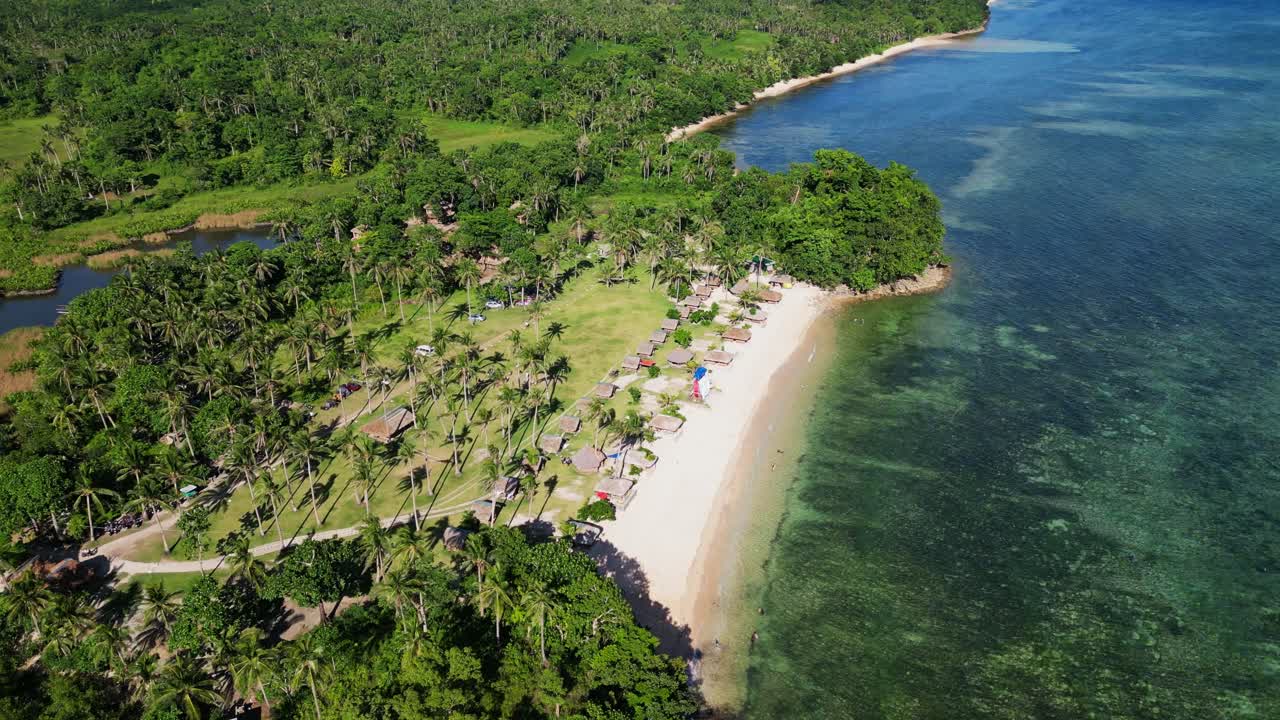 Aerial orbit of vibrant white sand Bagasbas Beach Resort with lush greenery and palm trees along pristine coastline at Catanduanes, Philippines.