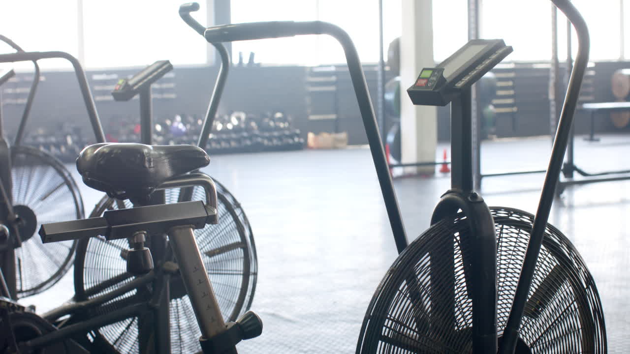 Several stationary bikes are in gym with large windows in background