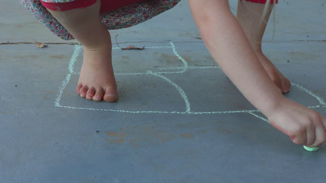 Girl draw with chalk hopscotch square patters on the floor, summer kids fun