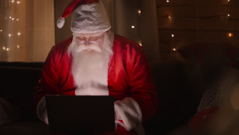 portrait: santa claus working on laptop sends or receives letters with wishes or congratulations by email for christmas or new year.