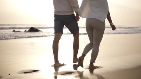 honeymoon married young couple on beach walking in love holding hands at romantic sunrise. woman and man relaxing on travel vacation holidays, wearing casual