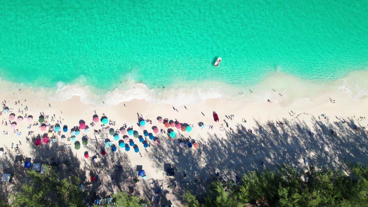 clip aéreo de 4k drone de playa de arena con agua esmeralda, olas rompiendo, sombrillas de colores