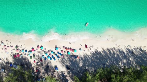 Overhead-4k-drone-clip-of-sandy-beach-with-emerald-water,-crashing-waves,-colorful-umbrellas