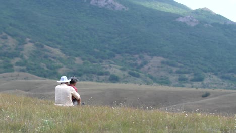 the boy is sitting on the lap of a hill