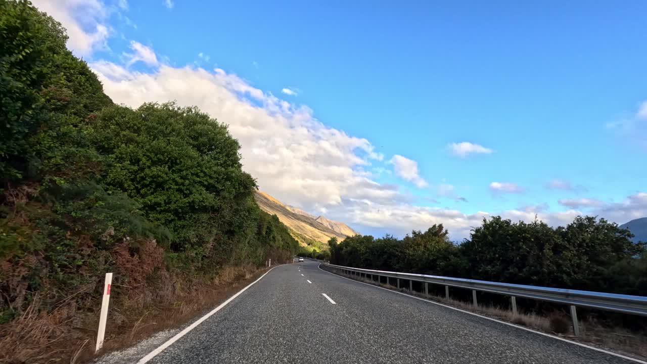 Vehicle travels winding lakeside road, mountain scenery, daylight, smooth camera movement, clear blue sky