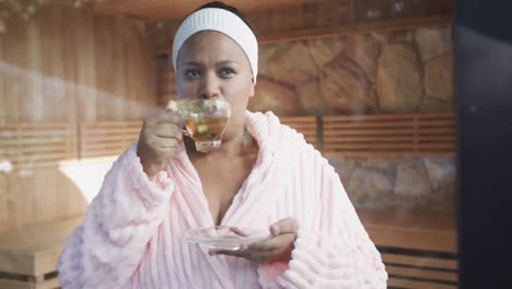 African-american-plus-size-woman-wearing-bathrobe-and-drinking-tea-at-spa,-unaltered,-slow-motion