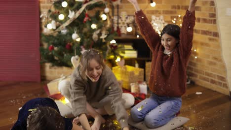 Mom-and-Daughters-catching-colored-confetti-in-hand-glad-laughing-near-Christmas-tree