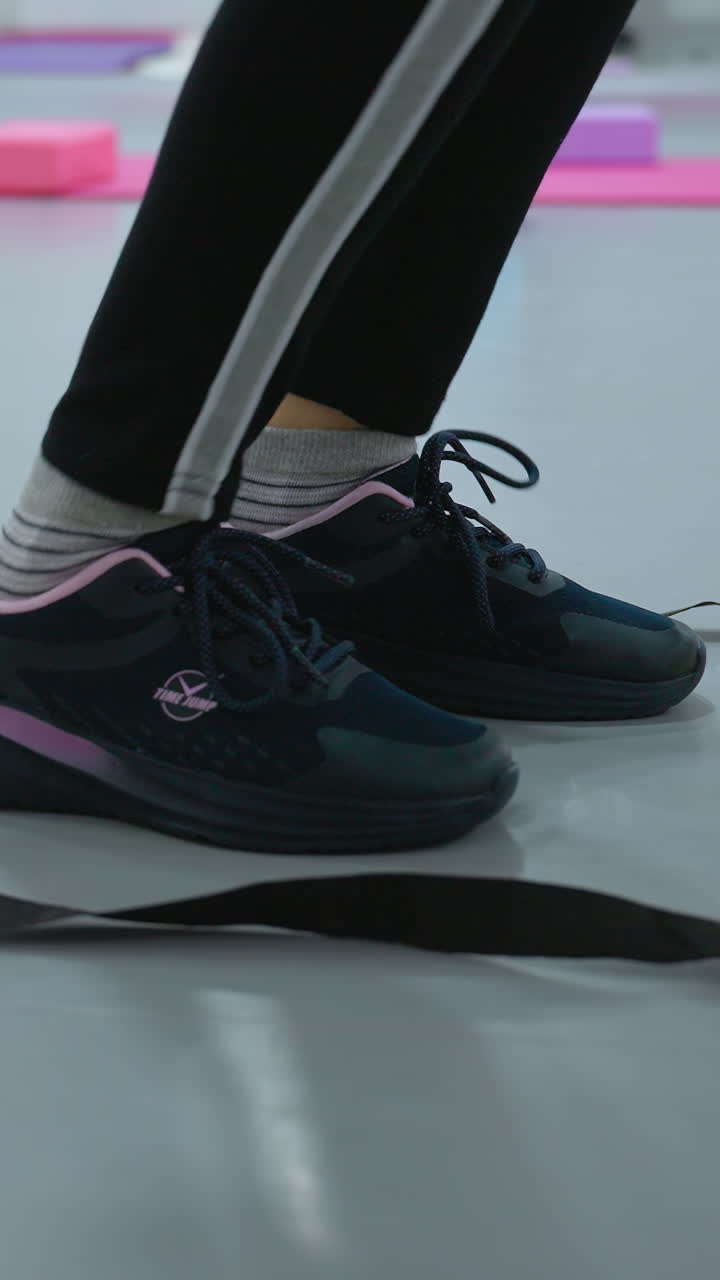 vista de cerca de la pierna de una persona en lienzo negro saltando a través de una escalera de agilidad en el piso del gimnasio, equipos de entrenamiento, esteras de fitness y accesorios de entrenamiento en el fondo